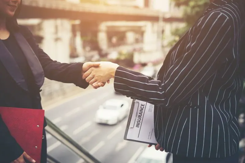 Two professionals shaking hands after a mediated settlement, one holding the signed papers