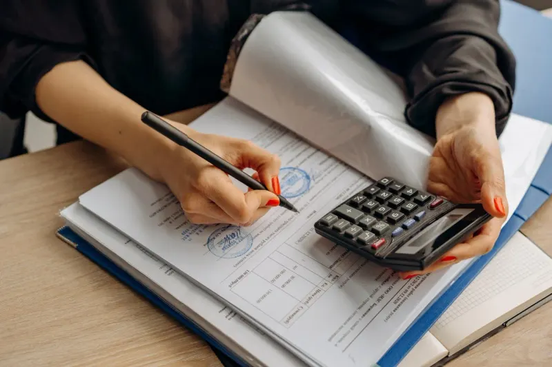 Business owner working a calculator over stamped financial records and contract pages