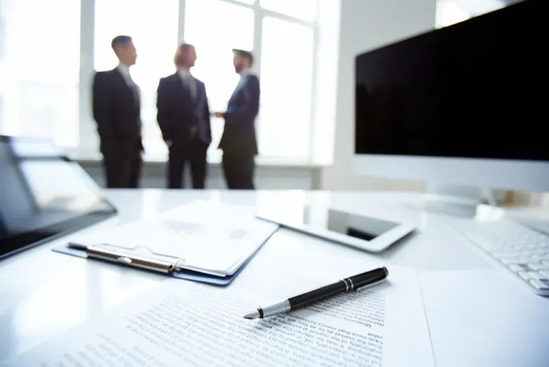 Three business people meeting in a bright office with contract papers and a pen on the desk