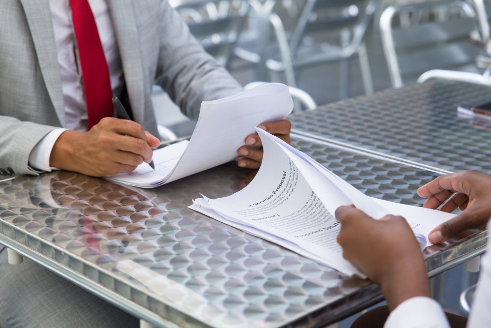Professional meeting between two individuals discussing nonprofit organization setup documents on a metal table.