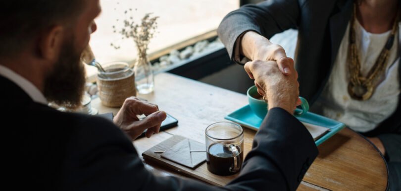 Business negotiation handshake over coffee in a modern café setting, illustrating partnership discussions and legal agreements relevant to business law services.