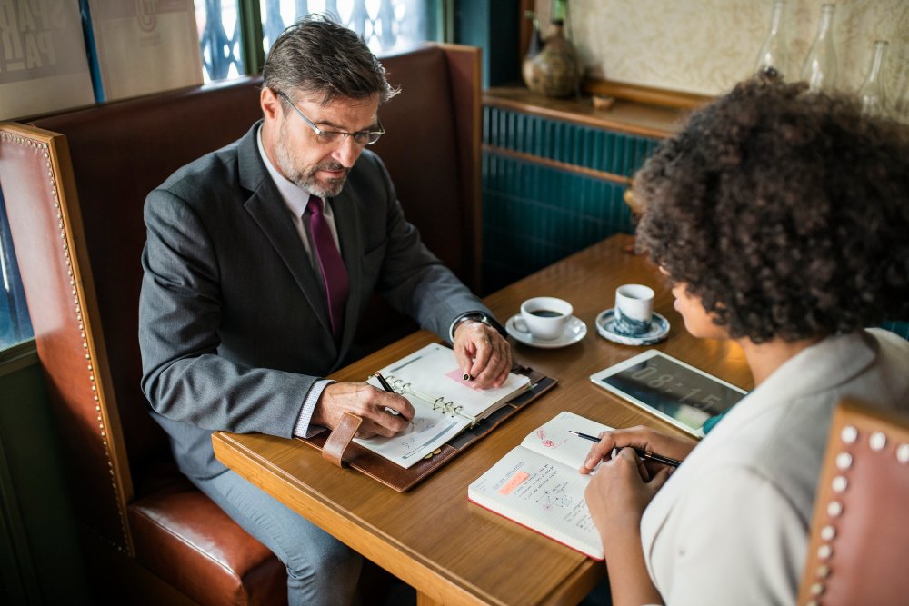 Business attorney consulting with client at table, discussing legal strategies and business formation, with coffee and notebooks present.