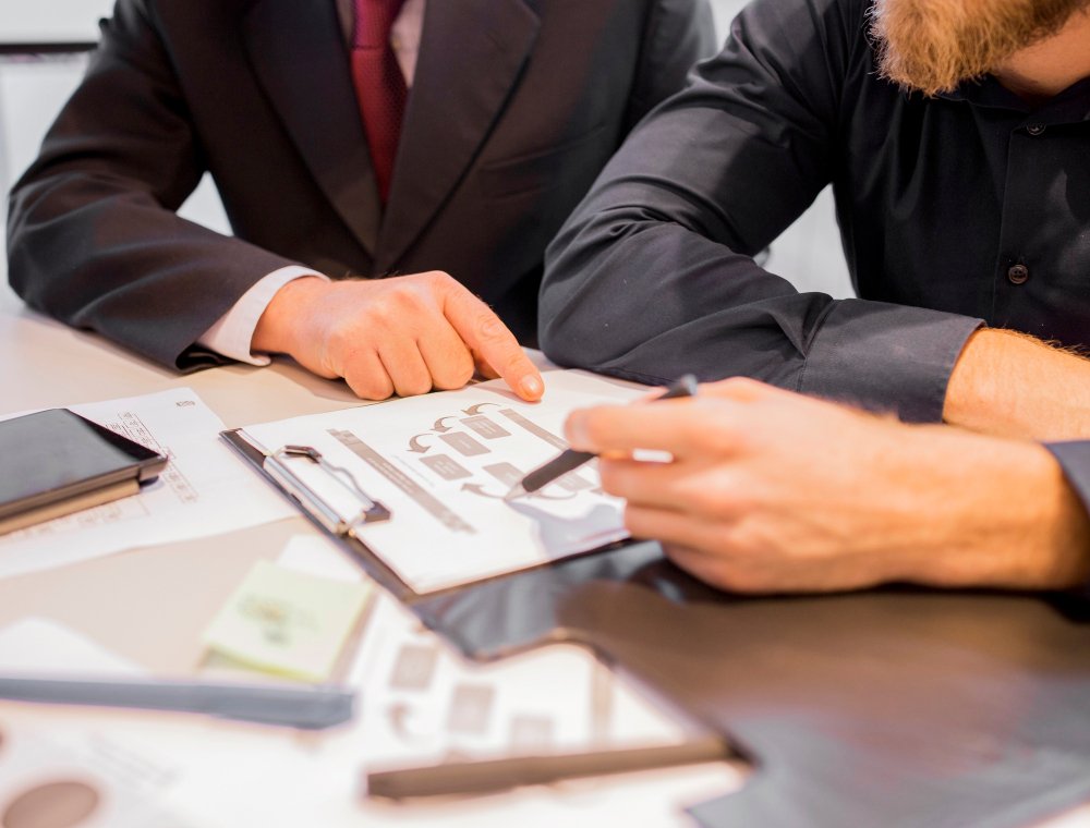 Business professionals discussing asset transfer agreements over a table, reviewing documents and charts related to financial and legal implications.