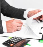 “Business Debt Collection Legal Support – Professional Debt Recovery Attorney in New Jersey” Person reviewing construction contracts with a pen and calculator on a desk, representing legal services in construction law in New Jersey.