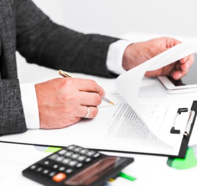 Business attorney reviewing legal documents and signing contracts at a desk with a calculator and clipboard, representing comprehensive legal services for businesses.