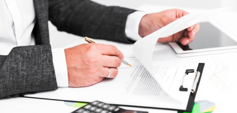 Business professional reviewing legal documents and taking notes, emphasizing contract negotiation and compliance in a corporate setting.