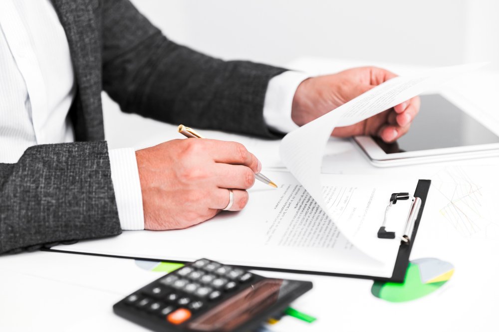 Business professional reviewing legal documents and drafting notes with a calculator and tablet on the desk, symbolizing business debt collection support.