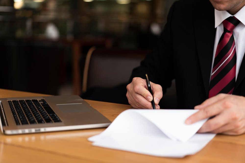 Business professional in a suit signing documents at a table with a laptop, symbolizing corporate formation and legal services for C-Corporations in New Jersey.