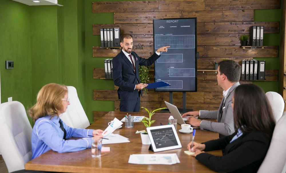 Business meeting with a man presenting a report on a digital screen, surrounded by colleagues discussing business entity formation services.