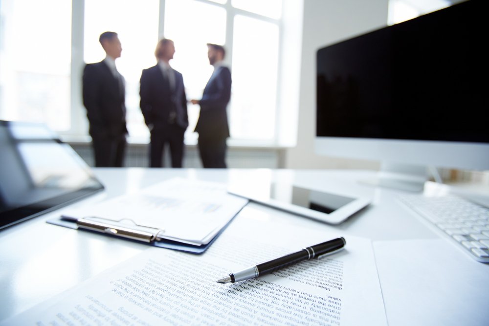 Business professionals discussing in a bright office, with documents and a pen on a desk, symbolizing business valuation guidance and legal services.