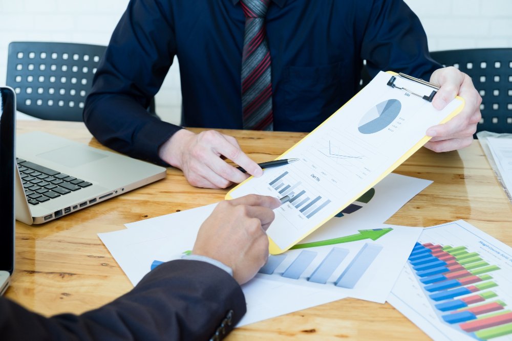 Business professionals discussing Stock Purchase Agreements, analyzing charts and graphs on a clipboard and documents during a meeting.