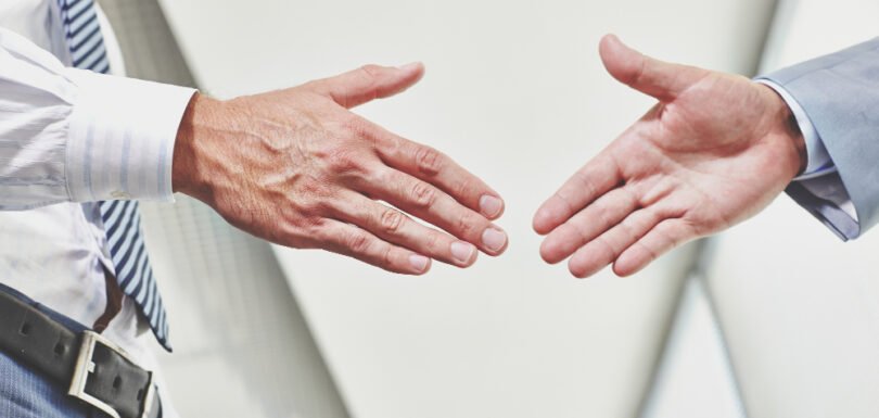 Hands of two business professionals about to shake hands, symbolizing agreement and collaboration in mergers and acquisitions.
