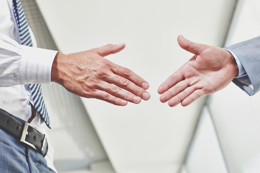 Hands of two business professionals reaching out for a handshake, symbolizing partnership and conflict resolution in business law.