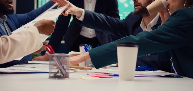 Business professionals engaged in a collaborative meeting, discussing documents and sharing ideas, with coffee cups and office supplies visible on the table, reflecting a dynamic work environment relevant to contract negotiations and dispute resolution.