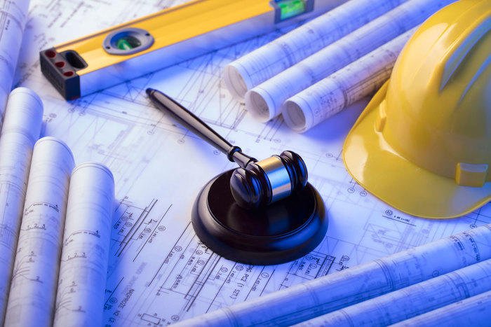 Construction law gavel on architectural blueprints with a yellow hard hat and level tool, symbolizing legal oversight in construction projects.
