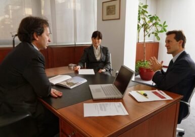 Business meeting at a law office with three professionals discussing legal matters, laptop and documents on the table, emphasizing business law services.