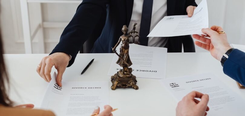 Hands of individuals discussing legal documents, including divorce decrees, with a statue of Lady Justice in the center, symbolizing legal guidance and the importance of formal agreements in business law.