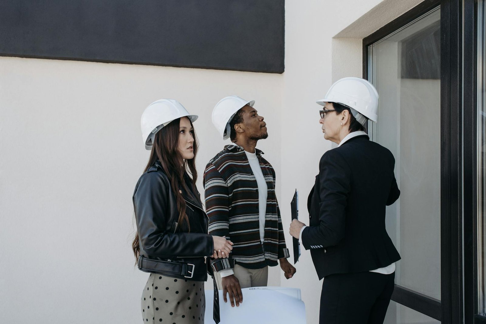Three construction professionals discussing contractor agreements, wearing hard hats, with building plans in hand, set against a neutral backdrop.