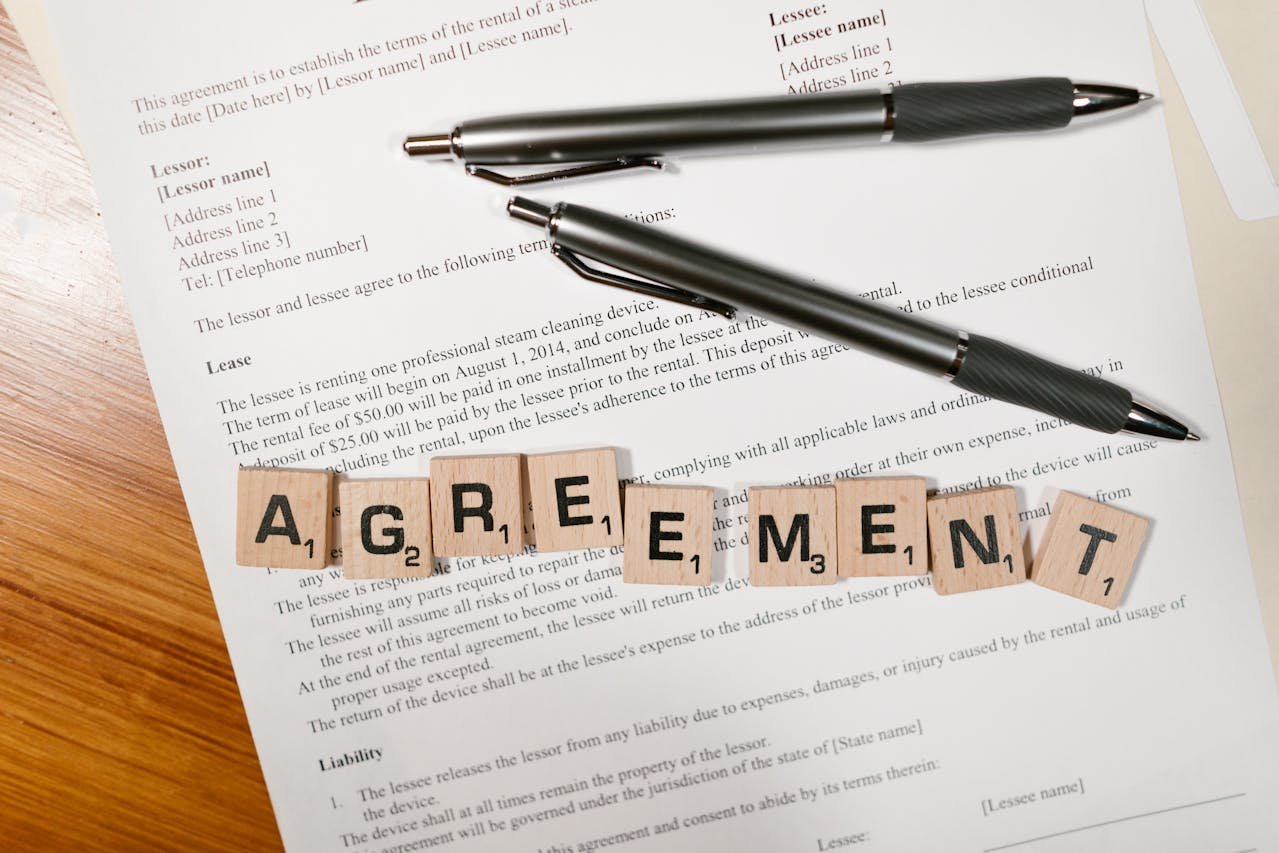 Scrabble tiles spelling "AGREEMENT" on a commercial lease document with two pens, emphasizing legal agreements in commercial leasing.