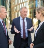 business-team-discussing-project-outdoors-men-woman-wearing-office-suits-standing-talking-outdoors-with-city-building-background-meeting-cooperation-concept_74855-6774